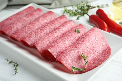 Photo of Slices of tasty smoked sausage and spices on white wooden table, closeup
