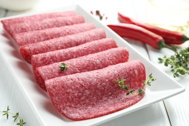 Photo of Slices of tasty smoked sausage and spices on white wooden table, closeup