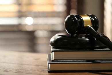 Photo of Judge's gavel, sound block and books on wooden table against blurred background, closeup. Space for text