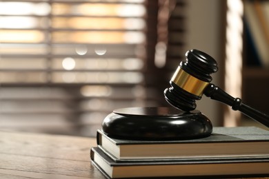 Photo of Judge's gavel, sound block and books on wooden table against blurred background, closeup. Space for text