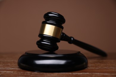 Photo of Judge's gavel and sound block on wooden table against brown background, closeup