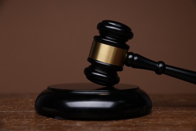 Photo of Judge's gavel and sound block on wooden table against brown background, closeup