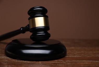 Photo of Judge's gavel and sound block on wooden table against brown background, closeup. Space for text