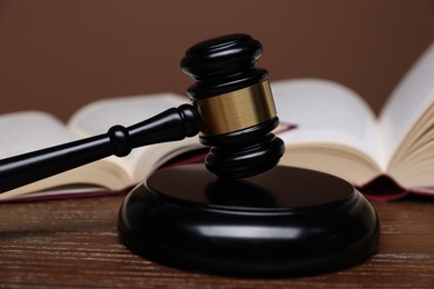 Photo of Judge's gavel, sound block and books on wooden table against brown background, closeup
