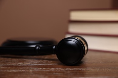 Photo of Judge's gavel, sound block and books on wooden table against brown background, closeup