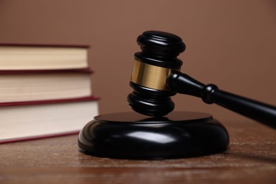Photo of Judge's gavel, sound block and books on wooden table against brown background, closeup