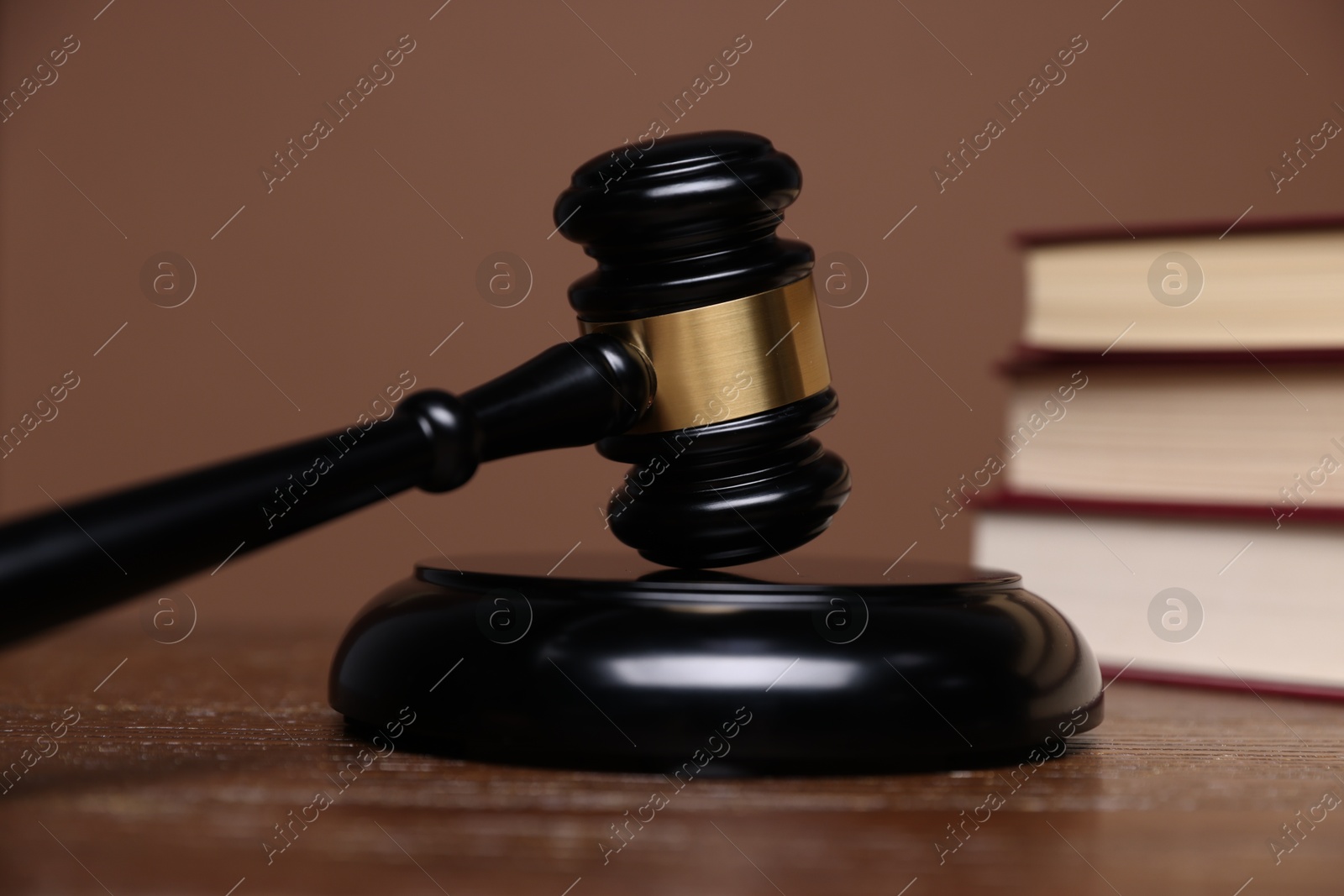 Judge's gavel, sound block and books on wooden table against brown background, closeup Photo of Judge's gavel, sound block and books on wooden table against brown background, closeup