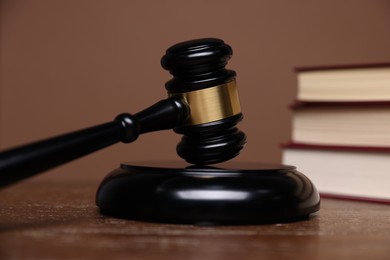 Photo of Judge's gavel, sound block and books on wooden table against brown background, closeup