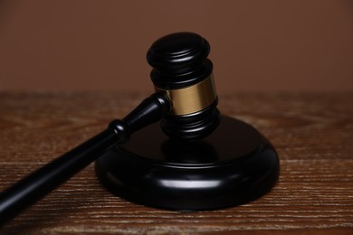 Photo of Judge's gavel and sound block on wooden table against brown background, closeup