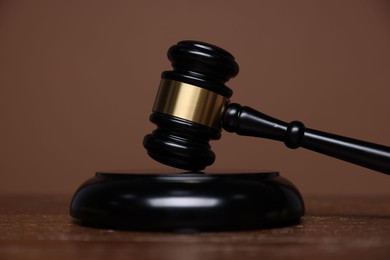 Photo of Judge's gavel and sound block on wooden table against brown background, closeup