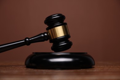 Photo of Judge's gavel and sound block on wooden table against brown background, closeup