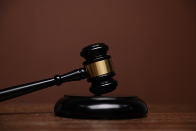 Photo of Judge's gavel and sound block on wooden table against brown background, closeup