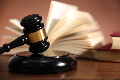Photo of Judge's gavel, sound block and books on wooden table against pale brown background, closeup