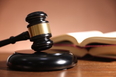 Photo of Judge's gavel, sound block and books on wooden table against pale brown background, closeup