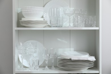 Photo of Clean glasses and plates on shelves near white wall indoors