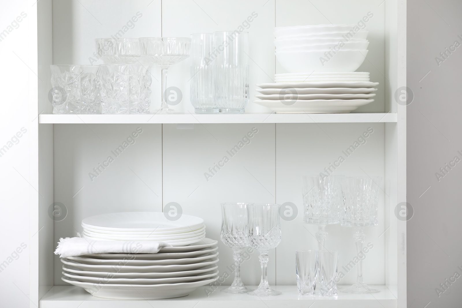 Clean glasses and plates on shelves near white wall indoors Photo of Clean glasses and plates on shelves near white wall indoors