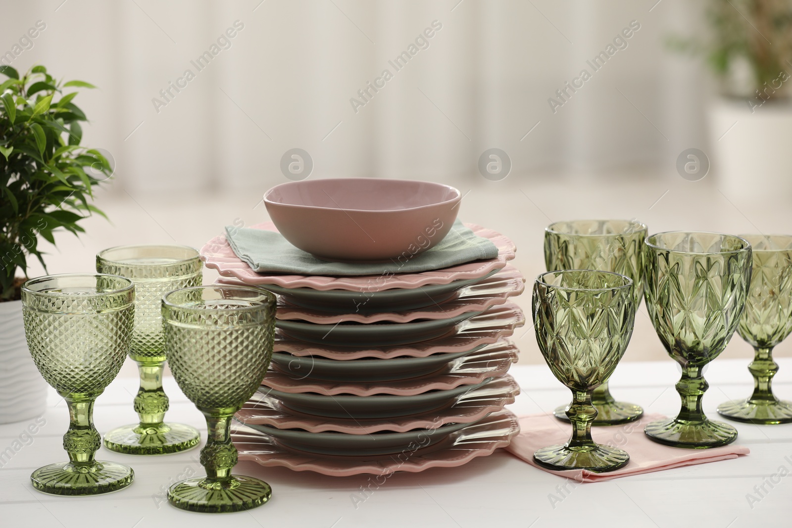 Photo of Clean glasses, plates and green houseplant on white wooden table indoors