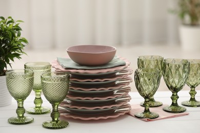 Photo of Clean glasses, plates and green houseplant on white wooden table indoors