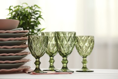 Photo of Clean glasses, plates and green houseplant on white wooden table indoors