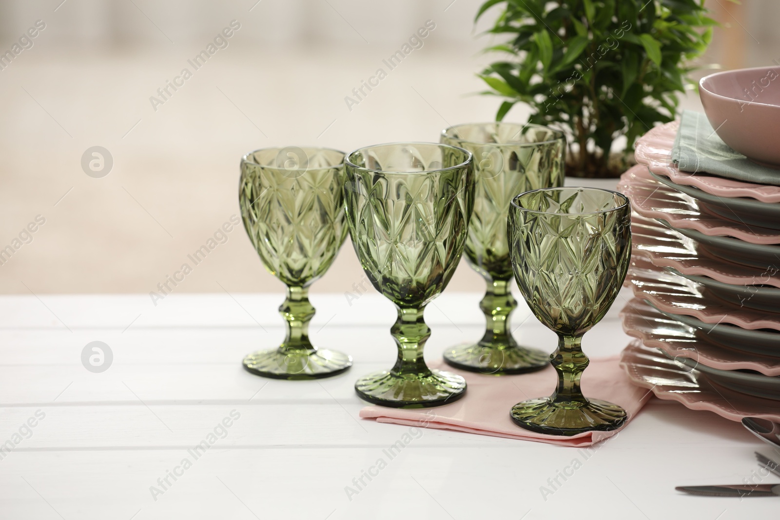 Clean glasses, plates and green houseplant on white wooden table indoors, space for text Photo of Clean glasses, plates and green houseplant on white wooden table indoors, space for text