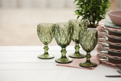 Photo of Clean glasses, plates and green houseplant on white wooden table indoors, space for text