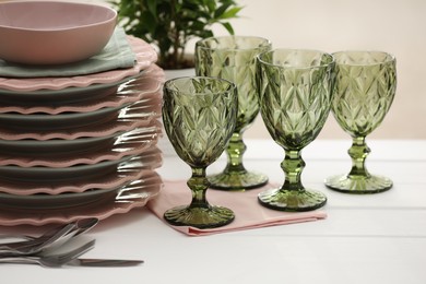 Photo of Clean glasses, plates, cutlery and green houseplant on white wooden table indoors