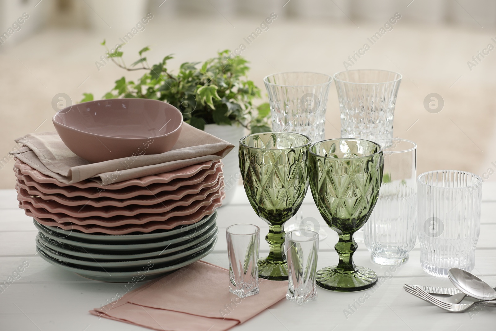 Clean glasses, plates, cutlery and green houseplant on white wooden table indoors Photo of Clean glasses, plates, cutlery and green houseplant on white wooden table indoors