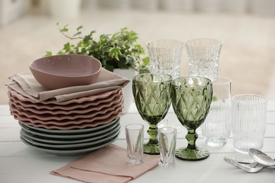 Photo of Clean glasses, plates, cutlery and green houseplant on white wooden table indoors