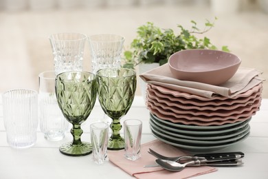 Photo of Clean glasses, plates, cutlery and green houseplant on white wooden table indoors
