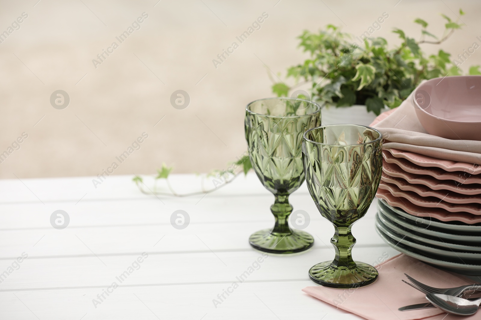Clean glasses, plates, cutlery and green houseplant on white wooden table indoors, space for text Photo of Clean glasses, plates, cutlery and green houseplant on white wooden table indoors, space for text