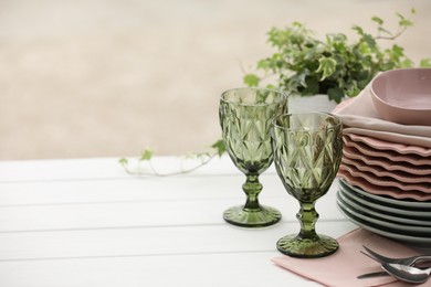 Photo of Clean glasses, plates, cutlery and green houseplant on white wooden table indoors, space for text