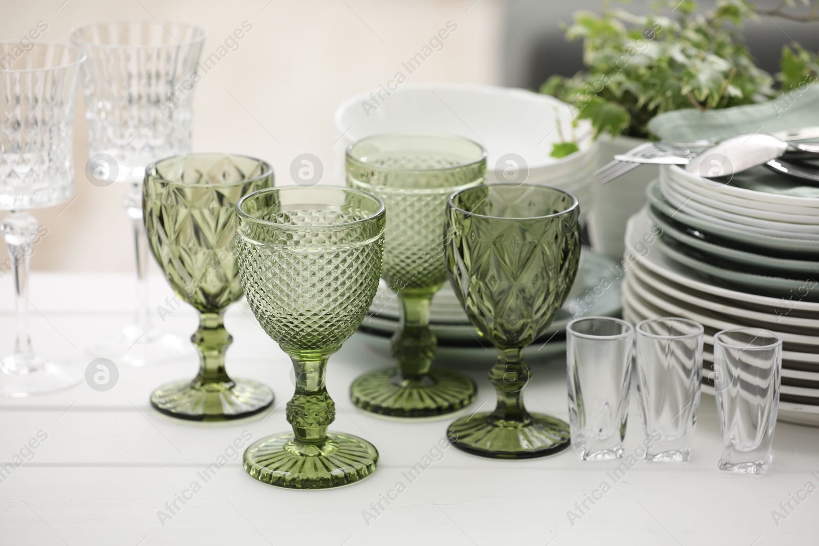 Clean glasses, plates, cutlery and green houseplant on white wooden table indoors Photo of Clean glasses, plates, cutlery and green houseplant on white wooden table indoors