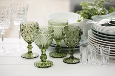 Photo of Clean glasses, plates, cutlery and green houseplant on white wooden table indoors