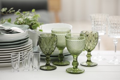 Photo of Clean glasses, plates, cutlery and green houseplant on white wooden table indoors
