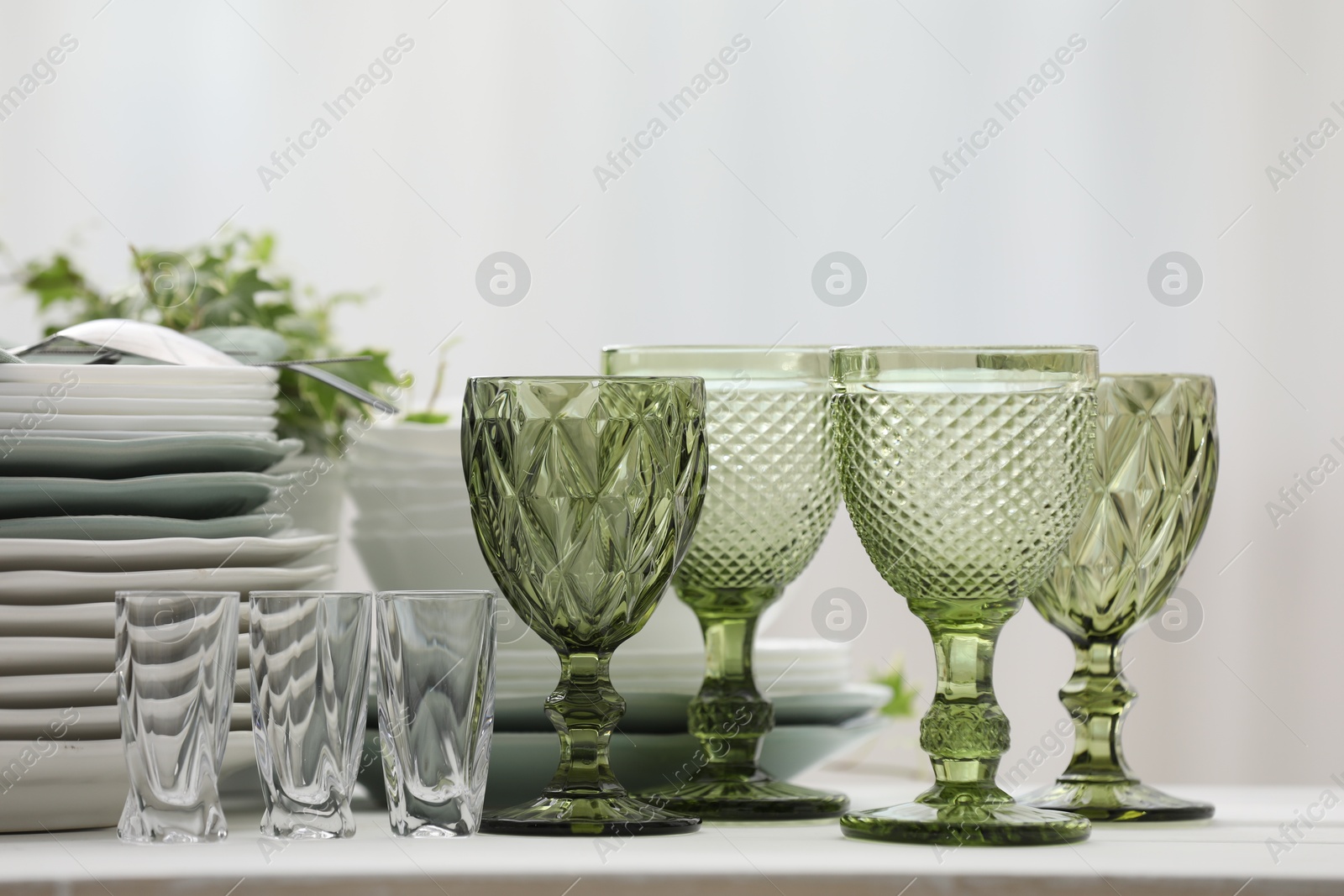 Clean glasses, plates, cutlery and green houseplant on white table indoors Photo of Clean glasses, plates, cutlery and green houseplant on white table indoors
