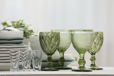 Photo of Clean glasses, plates, cutlery and green houseplant on white table indoors