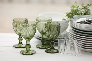 Photo of Clean glasses, plates, cutlery and green houseplant on white wooden table indoors