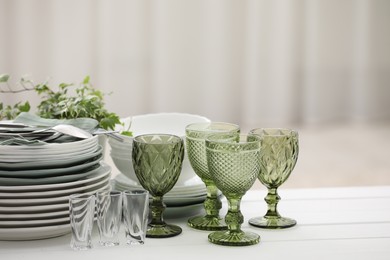 Photo of Clean glasses, plates, cutlery and green houseplant on white wooden table indoors
