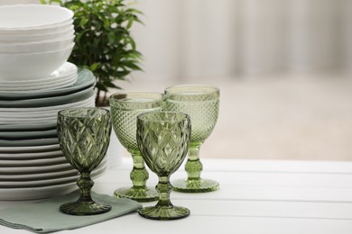 Photo of Clean glasses, plates and green houseplant on white wooden table indoors, space for text