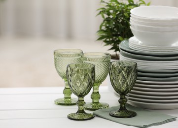 Photo of Clean glasses, plates and green houseplant on white wooden table indoors, space for text