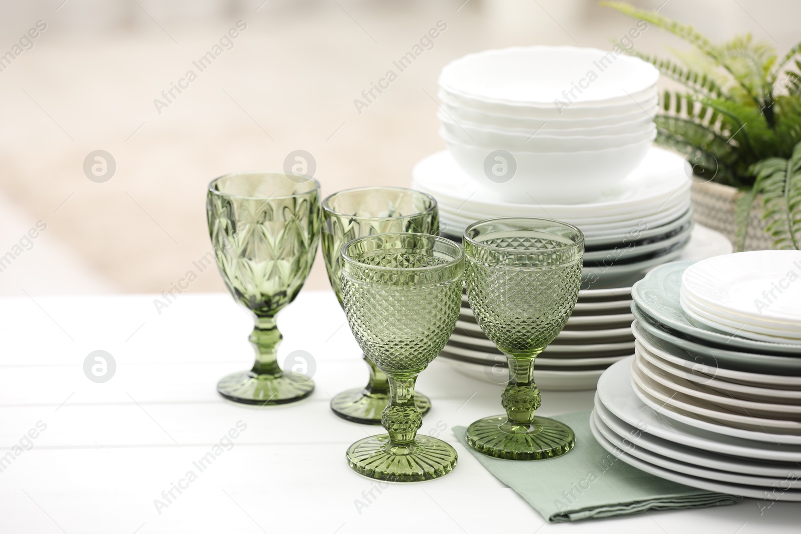 Clean glasses, plates and green houseplant on white wooden table indoors, space for text Photo of Clean glasses, plates and green houseplant on white wooden table indoors, space for text