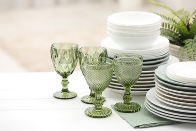 Photo of Clean glasses, plates and green houseplant on white wooden table indoors, space for text