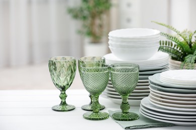 Photo of Clean glasses, plates and green houseplant on white wooden table indoors, space for text