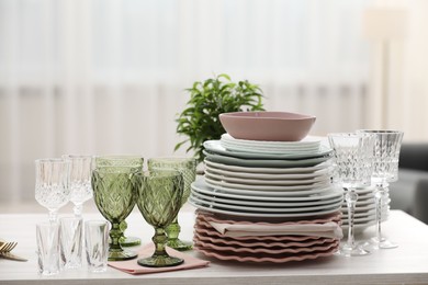 Photo of Clean glasses, plates and green houseplant on white wooden table indoors