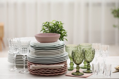 Photo of Clean glasses, plates and green houseplant on white wooden table indoors