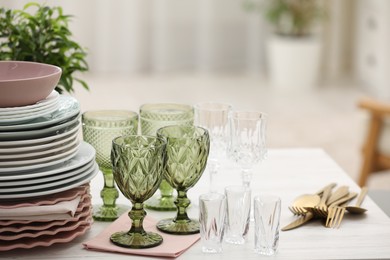 Photo of Clean glasses, plates, cutlery and green houseplant on white wooden table indoors