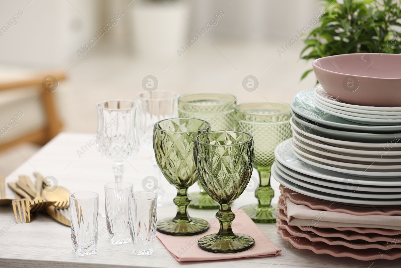 Clean glasses, plates, cutlery and green houseplant on white wooden table indoors Photo of Clean glasses, plates, cutlery and green houseplant on white wooden table indoors