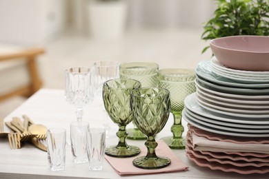 Photo of Clean glasses, plates, cutlery and green houseplant on white wooden table indoors