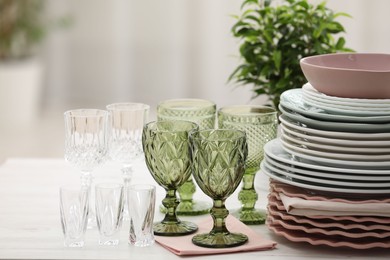 Photo of Clean glasses, plates and green houseplant on white wooden table indoors