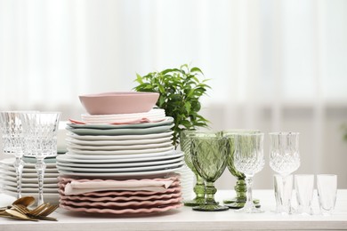 Photo of Clean glasses, plates, cutlery and green houseplant on white wooden table indoors